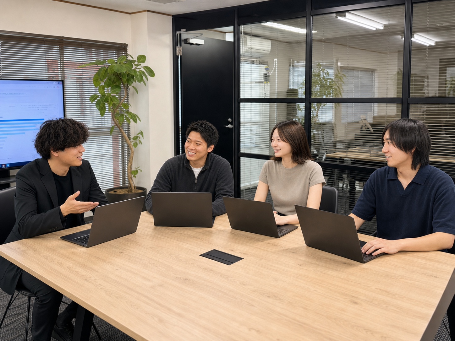 WE株式会社の4名がノートPCを開き、互いに顔を向けて談笑しながら仕事をする様子